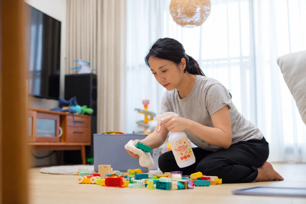 Parent wiping plastic and wooden baby toys on a play mat with natural spray cleaner