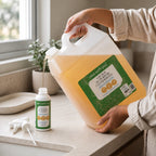 Person pouring Clean Earth natural 10L all-purpose cleaner refill into a 500ml spray bottle on a bright kitchen counter.